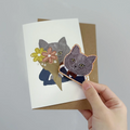 All occasion card with cat illustrations and a hand holding it against a gray background