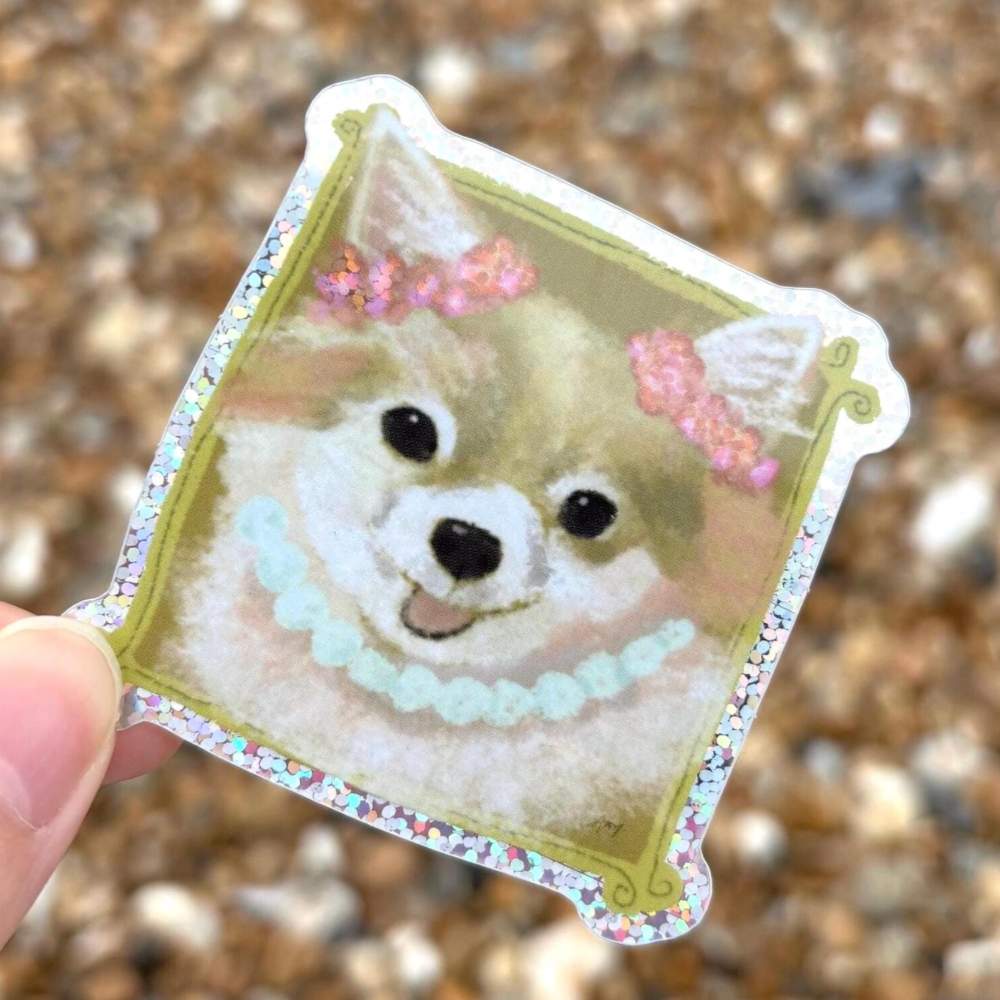 Glitter sticker of a Chihuahua with decorative elements held against a blurred natural background