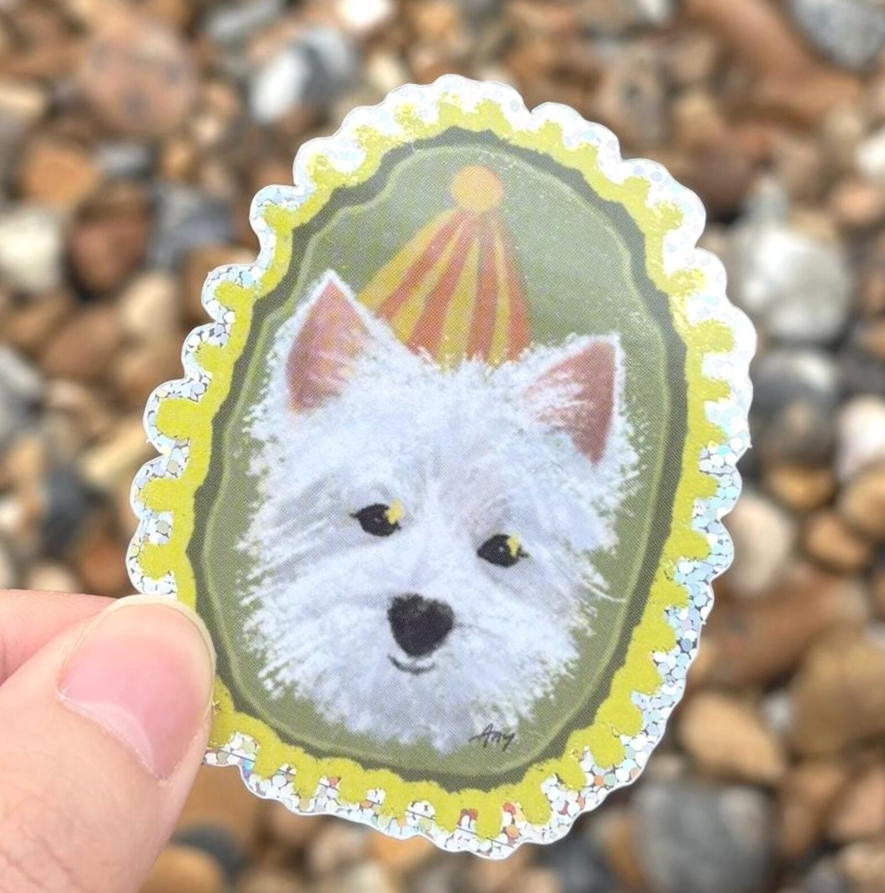 Sticker of a Westie white dog with a yellow border held against a pebbly background